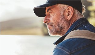 Senior man in a cap staring into the distance near a lake funeral plans