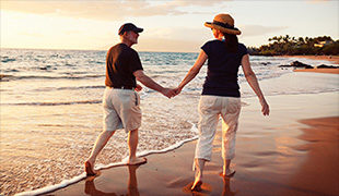 Couple in hats holding hand and walking in the surf of a beach best funeral plans